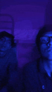 a man is sitting on a bed in a dark room with a blue light behind him .