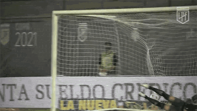 a soccer goalie dives to catch a soccer ball in front of a banner that says 2021