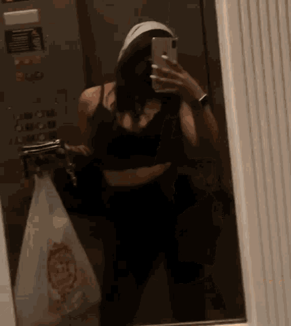 a woman is taking a selfie in an elevator while holding a bag of food .