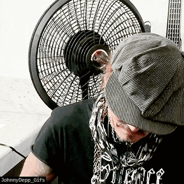 a man wearing a hat and a johnny depp gifs shirt stands in front of a fan