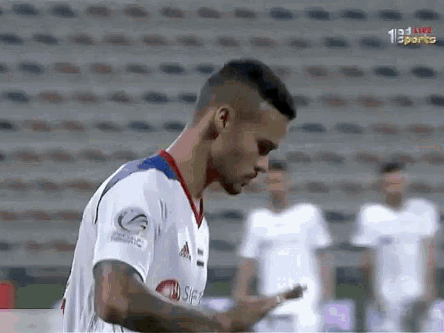 a soccer player wearing a white adidas jersey looks down at his phone