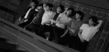 a black and white photo of a group of men laying on top of a couch .