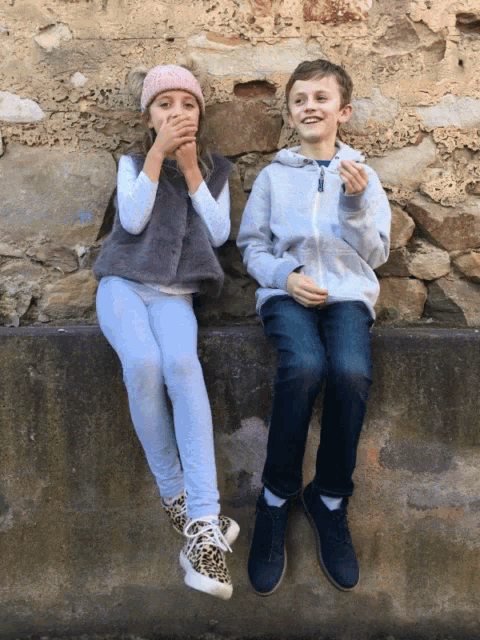 a boy and a girl are sitting on a stone wall eating food