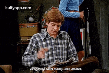 a man in a plaid shirt is reading a newspaper and saying `` everything costs money . gas , clothes . ''