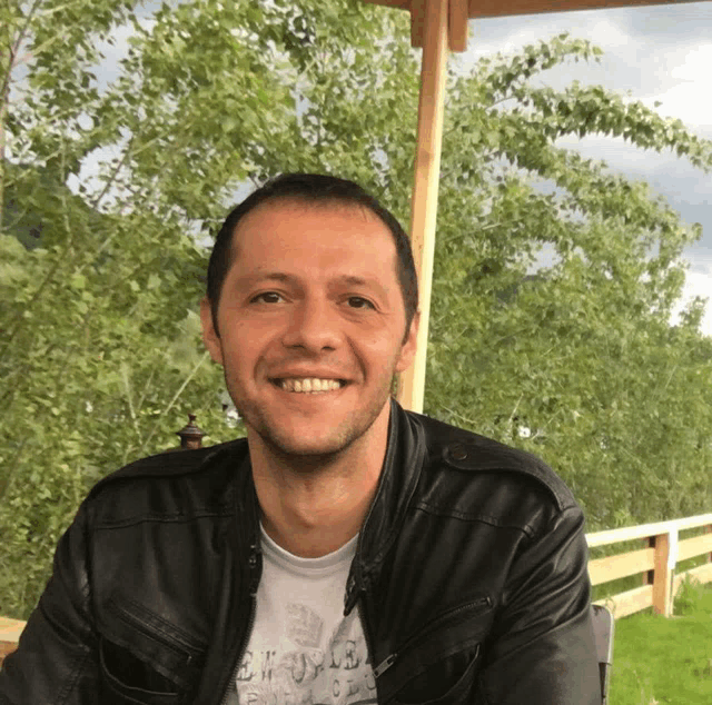 a man wearing a leather jacket and a shirt that says ' a ' on it smiles