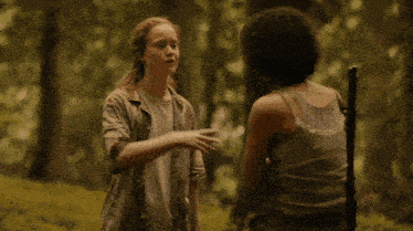 two women are standing in the woods and one has a gun