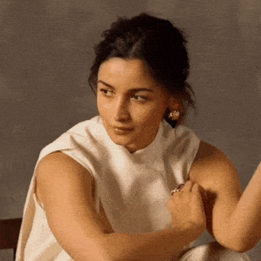 a woman wearing a white top and gold earrings looks to the side