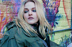 a woman in a green jacket is standing in front of a brick wall .