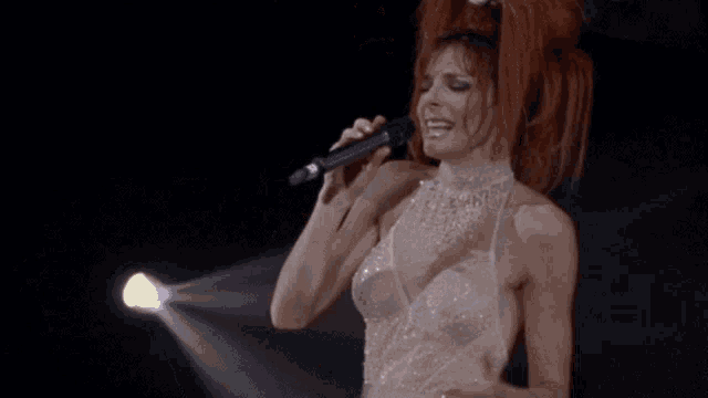 a woman with red hair singing into a microphone while wearing a clear dress