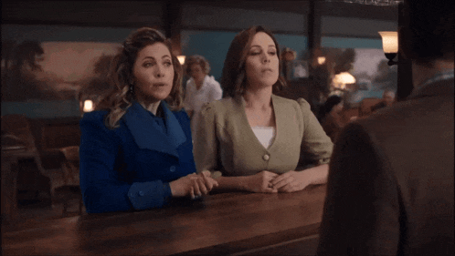 two women are sitting at a counter and one is pointing