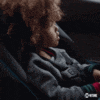 a little girl is sitting in a car seat and making a shhh gesture .