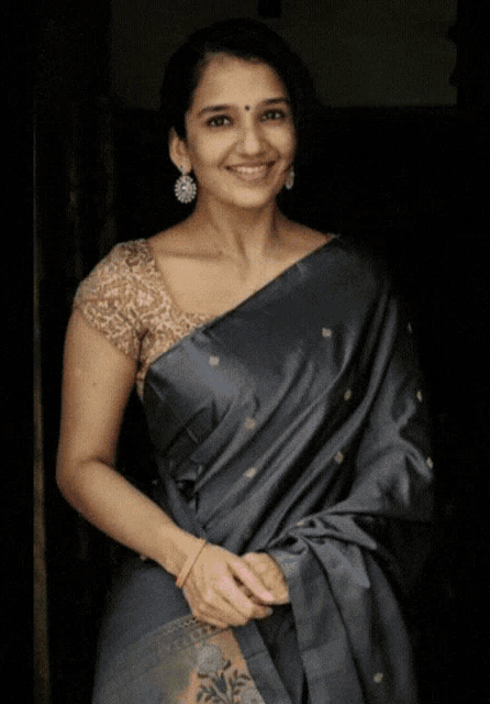 a woman wearing a blue saree and a gold blouse smiles