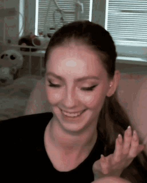 a woman in a black shirt is smiling and waving at the camera