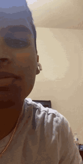 a close up of a man 's face with a white shirt and a gold chain around his neck