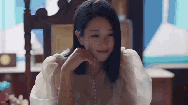 a woman in a white dress is sitting in a chair with her hand on her chin and smiling .