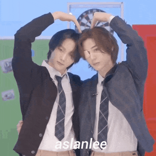 two young men are making a heart shape with their hands while standing next to each other .