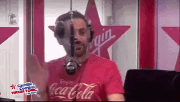 a man wearing a red coca cola shirt stands in front of a virgin radio station
