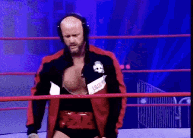 a wrestler wearing headphones and a jacket with a skull on it is standing in a ring .