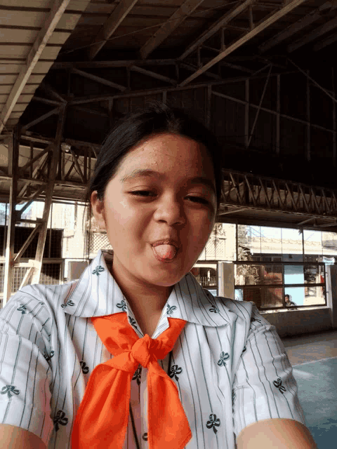 a girl wearing a striped shirt and an orange tie making a funny face