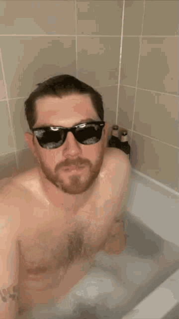 a shirtless man wearing sunglasses is taking a bath in a bathtub