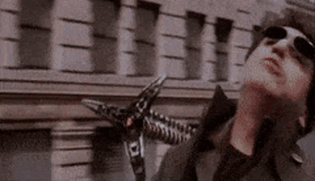 a man wearing sunglasses is standing in front of a building holding a skeleton arm .