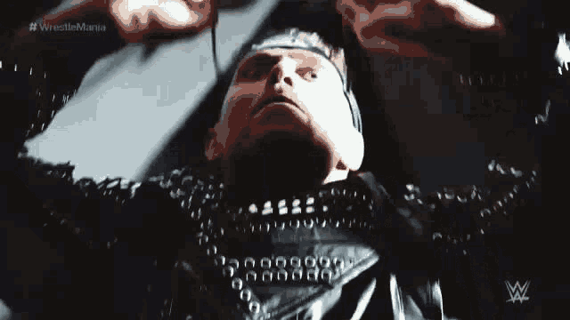 a man wearing a leather jacket and a crown is standing in a dark room with his arms outstretched .
