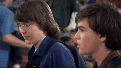 two boys are sitting next to each other and one has a backpack on his back