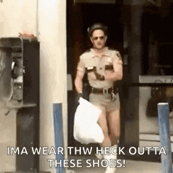 a man in a sheriff 's uniform is carrying a bag of trash and talking on a phone .