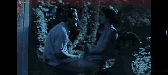 a man is holding a woman in his arms in a dark room with a newcut logo on the bottom right