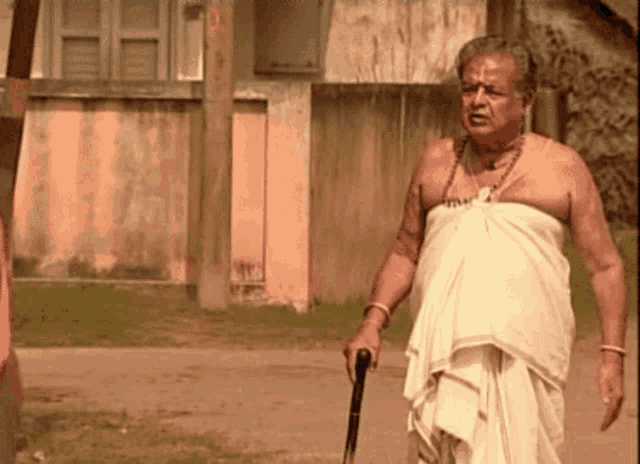 a man in a white towel holds a cane in front of a building