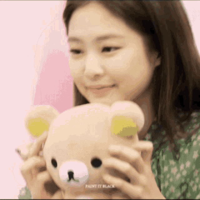 a woman in a green dress is holding a teddy bear in her hands .