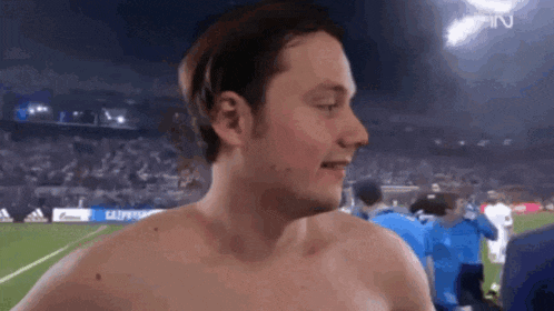 a man without a shirt is standing on a soccer field .