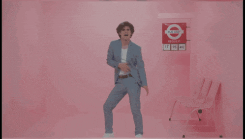 a man in a suit is dancing in front of a pink wall that says i need your love