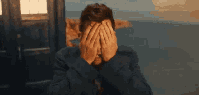 a man in a suit is covering his face with his hands and looking surprised