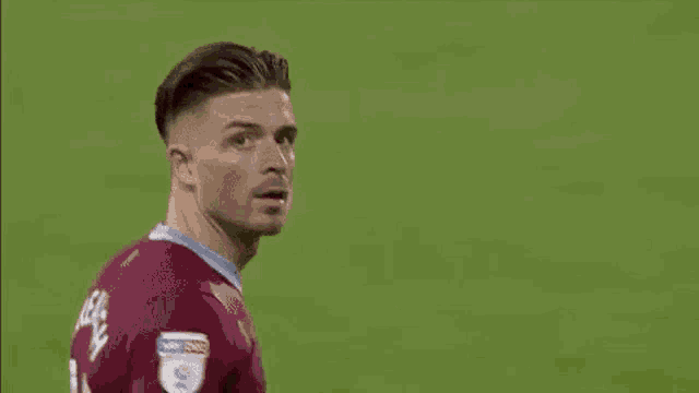 a soccer player wearing a maroon jersey is standing on a field with his hand on his head .
