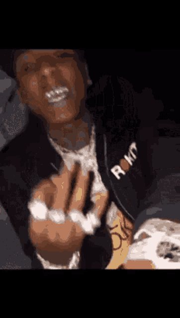 a close up of a man giving the middle finger while wearing a jacket with the letter r on it .