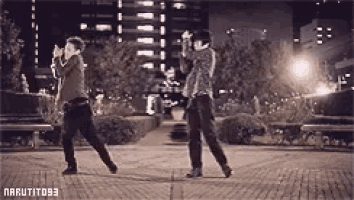 a black and white photo of two men dancing in a park at night .