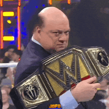 a bald man in a suit is holding a wrestling belt with the letter w on it
