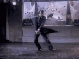 a man is dancing in the rain with an umbrella in front of a building .