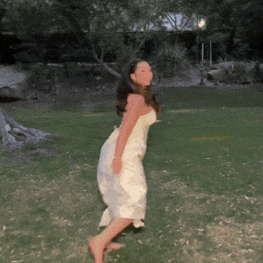 a woman in a white dress is dancing barefoot in the grass