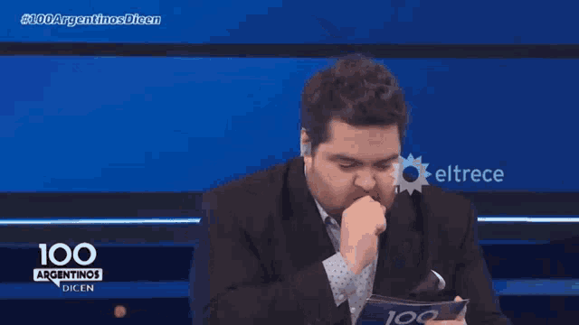 a man in a suit is sitting in front of a 100 argentinas dien sign