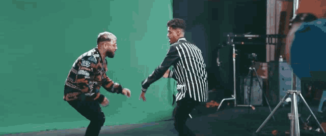 two men are dancing in front of a green screen and one has a sweater that says ' gucci ' on it