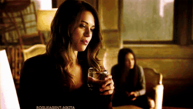 a woman is holding a glass of wine in a living room with rogueagent-nikita written on the bottom