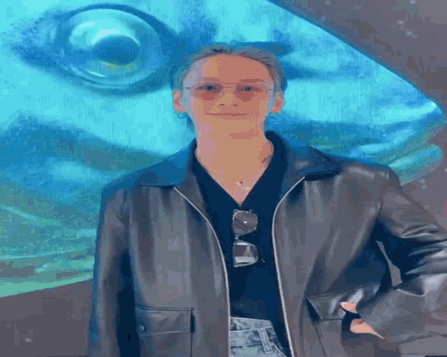 a man wearing sunglasses and a leather jacket is standing in front of a blue eye .