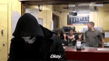 a man in a hooded jacket says okay in front of a group of people
