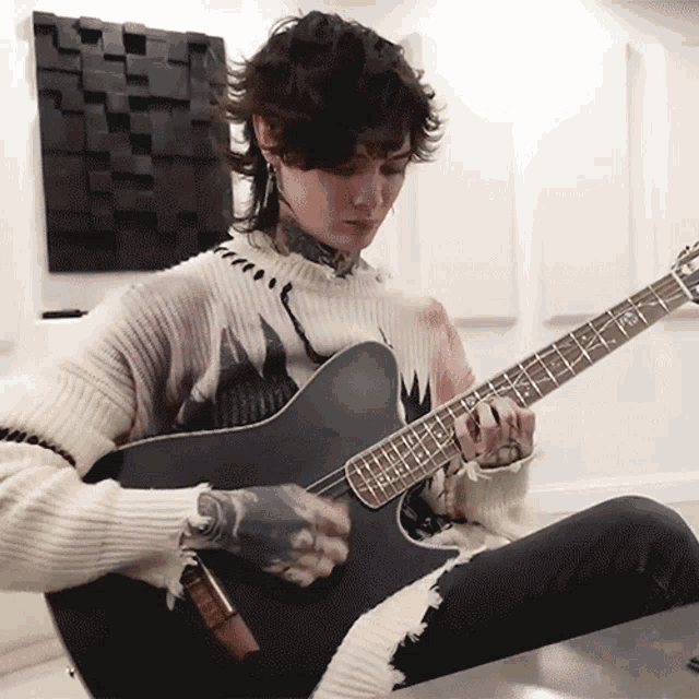 a man in a sweater is playing a guitar with a tattoo on his arm