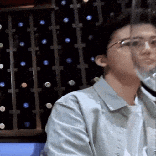 a man wearing glasses is sitting in front of a wall of wine bottles