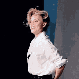 a woman wearing a white shirt and black pants is smiling with her hands behind her back .