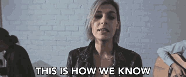 a woman singing in front of a brick wall with the words " this is how we know "