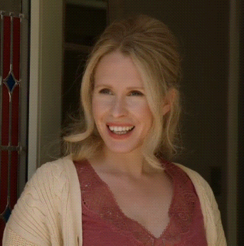 a woman wearing a pink top and a white sweater smiles